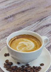 white cup with black coffee with milk. Handful of coffee beans on a wooden table. vertical view of drink with coffee. Copy space close up.