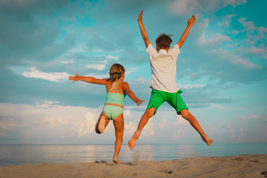 happy little boy and girl play on beach, kids jump from joy