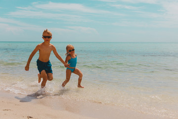 kids- girl and boy run play with waves on beach