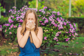 Young pretty woman blowing nose in front of blooming tree. Spring allergy concept