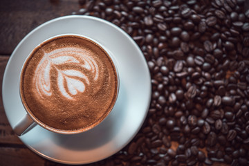 Latte art coffee with coffe beans on the table in vintage tone