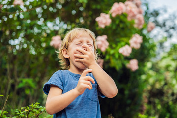 Boy blowing nose in front of blooming tree. Spring allergy concept. Children's allergies