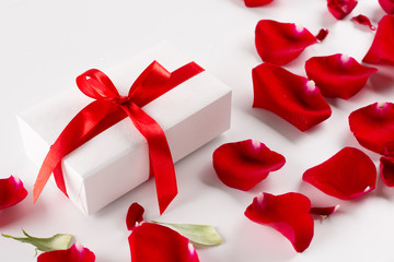 White gift box with red ribbon red velvet rose petals on white background. Top view