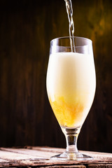 Cold beer is pouring into a glass forming foam.