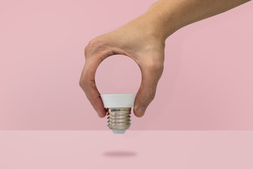 Hand holding a light bulb shape isolated on pink background, minimal idea