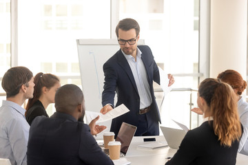 Confident coach giving handout to diverse seminar participants