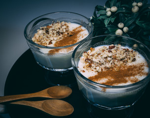 Rice pudding served in glass cups. Decorated. Close-up. Homemade dessert decorated with flower on black tray.
