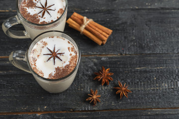 Homemade tea latte with cinnamon and anise on wooden rustic black background in glass mug