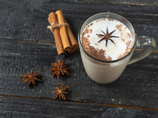Homemade tea latte with cinnamon and anise on wooden rustic black background in glass mug