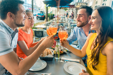 Two happy young couples toasting while sitting together at restaurant