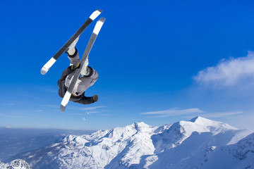 Extreme Jumping skier at jump above mountains at sunny day