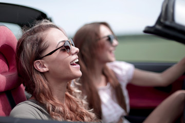 two fashionable girls travel in a convertible car.