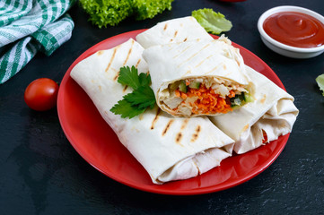 Delicious shawarma sandwich on a black background. Burritos wraps with grilled chicken and vegetables, greens. Fajitas, pita bread. Traditional Middle Eastern appetizer. Mexican cuisine