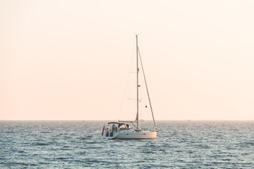 Little white boat floating on the water towards the horizon in the rays of the setting sun