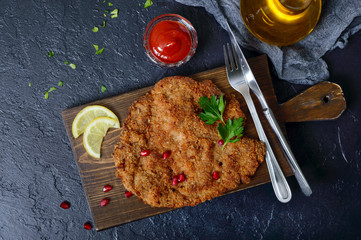 Large Viennese schnitzel on a black background. Meat dish. Top view, flat lay.