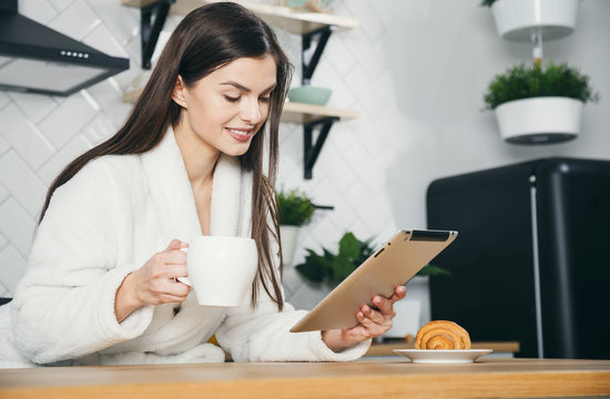 Young woman using a tablet computer to read the news and some emails while having breakfast at home - Powered by Adobe
