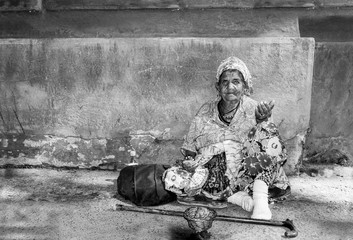 Old homeless Gypsy beggar woman with wrinkled face skin begging for money on the street in the city and looking in the camera with sad blue eyes social documentary concept real people black and white