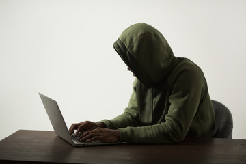 silhouette of a man in a hood sitting at a table with a laptop