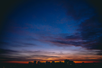 Cityscape with vivid warm dawn. Amazing dramatic blue violet cloudy sky above dark silhouettes of...