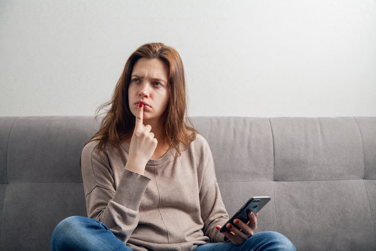  Attractive girl sitting on the sofa and communicates online by phone.