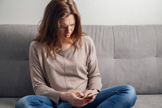  Attractive girl sitting on the sofa and communicates online by phone.
