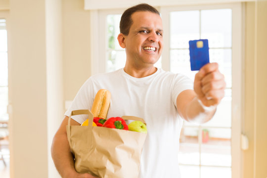 Middle age man holding groceries bag and showing credit card