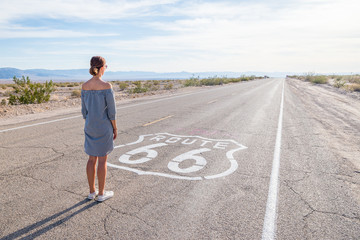 Young woman standing on an endless straight empty road in the middle of nowhere on the Route 66...