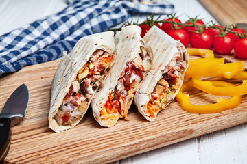 Close up view on delicious cuted shaurma or shawerma on board on white background. Shaurma with spices, cherry tomato and bell pepper. Arab or Eastern cuisine food with copy space. Fastfood kebab