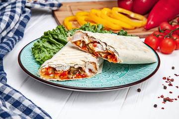 Close up view on delicious cuted shaurma or shawerma on blue plate on white background. Shaurma with spices, cherry tomato and bell pepper. Arab or Eastern cuisine food with copy space. Fastfood kebab