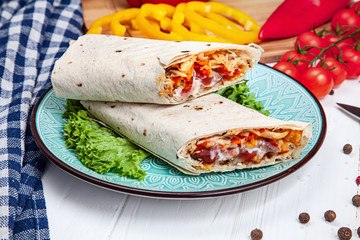 Close up view on delicious cuted shaurma or shawerma on blue plate on white background. Shaurma with spices, cherry tomato and bell pepper. Arab or Eastern cuisine food with copy space. Fastfood kebab