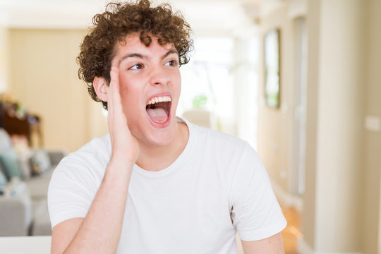 Young handsome man wearing white t-shirt shouting and screaming loud to side with hand on mouth. Communication concept.