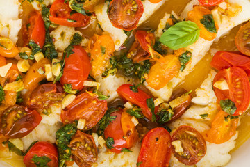 Baked cod fillet with cherry tomato and basil sauce, top view, close-up