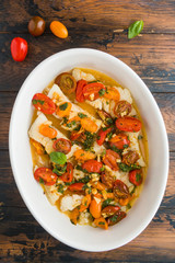 Fried cod fillet with cherry tomato and basil sauce in white dish on wooden rustic table, top view