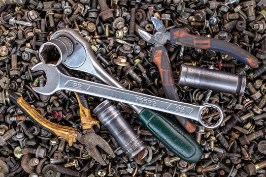 Flat Lay metal wrenches, ratchet, pliers, interchangeable tool heads of different sizes lie on the background of various metal cogs, screws and nails, top view. Close-up Carpenter's Tool Kit
