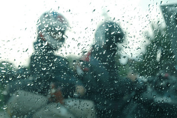 Motorcycle riders in the rain through a window with rain drops