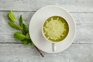 cup of hot matcha green tea latte and mint on grey wooden background