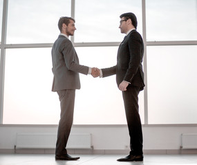 businessmen shake hands, standing near a large office window