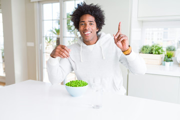 African American man eating fresh green peas at home surprised with an idea or question pointing finger with happy face, number one