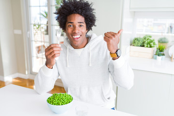 Fototapeta na wymiar African American man eating fresh green peas at home pointing and showing with thumb up to the side with happy face smiling