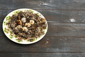 Open eco-friendly ceramic plate with feathers and quail eggs on rough dyed wooden background. Eggs For Easter. Boho stile.