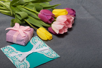 Bouquet of tulips of different colors on a gray background. Next greeting card and gift wrapped.