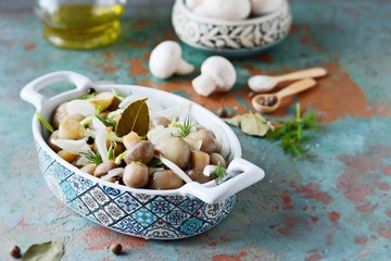 Delicious marinated mushrooms in a beautiful bowl with onions, pepper, dill and olive oil on a gray-blue background, top view, champignons