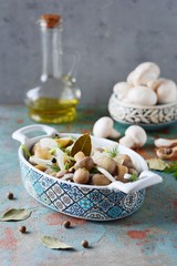 Delicious marinated mushrooms in a beautiful bowl with onions, pepper, dill and olive oil on a gray-blue background, top view, champignons