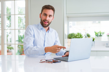 Handsome business man working using computer laptop very happy pointing with hand and finger