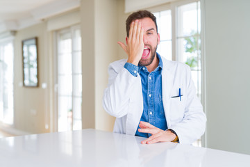Fototapeta premium Handsome doctor man wearing medical coat at the clinic covering one eye with hand with confident smile on face and surprise emotion.