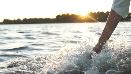 At sunset, close-up the hand of a girl moving through the water