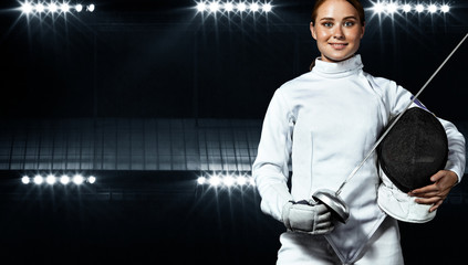 Young fencer athlete wearing fencing costume holding the sword and mask. Black background with...