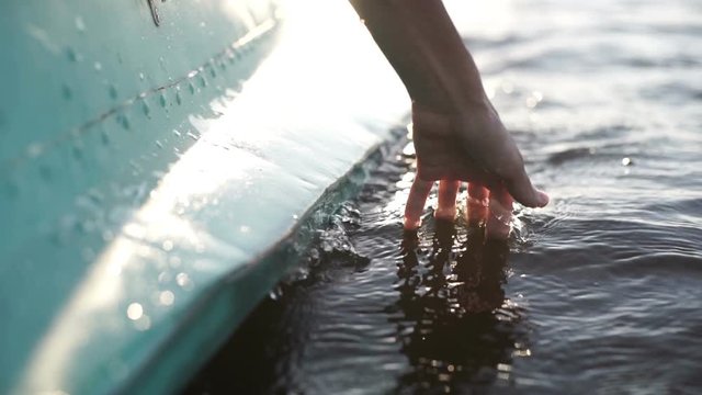 At sunset, close-up the hand of a girl moving through the water