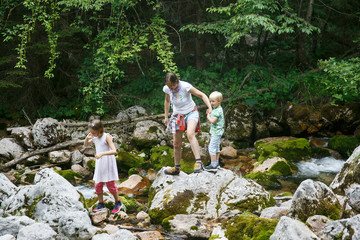 Mother with children having fun, playing by a mountain creek in summer.