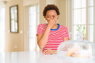 Young beautiful african american woman at home smelling something stinky and disgusting, intolerable smell, holding breath with fingers on nose. Bad smells concept.